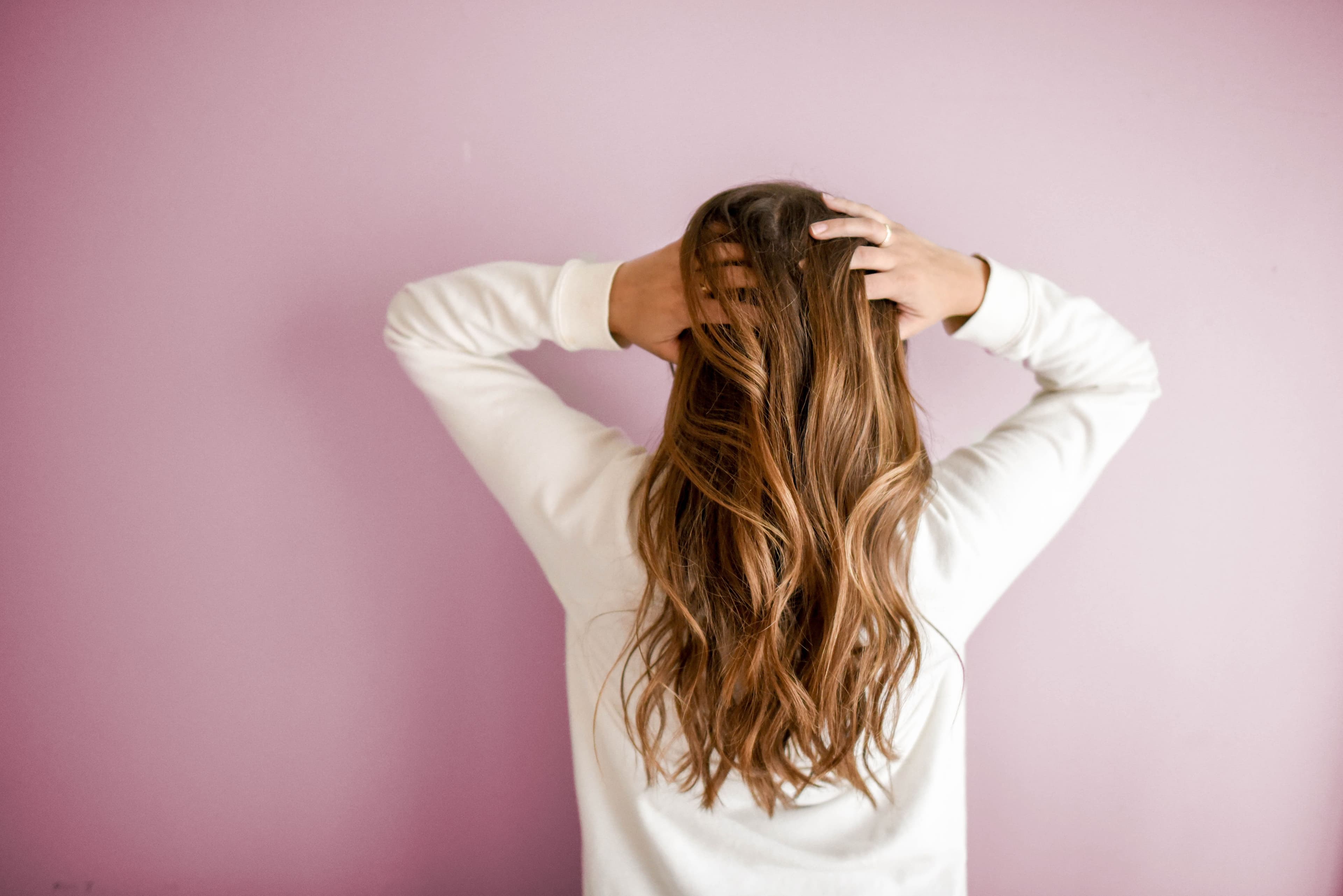 A woman standing with her hands in her long hair and her back facing the camera.