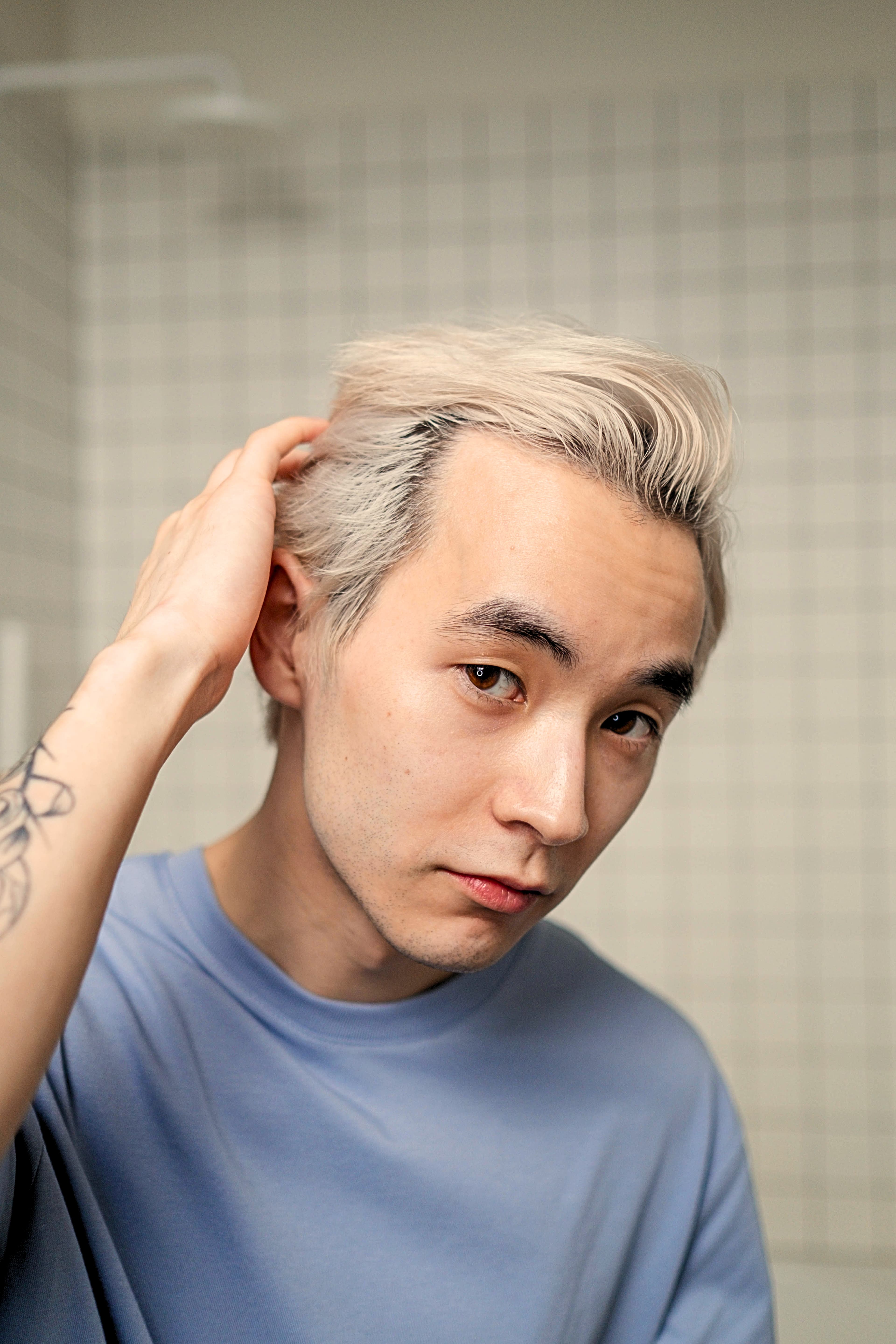 A man wearing a blue shirt is running his fingers through his hair.