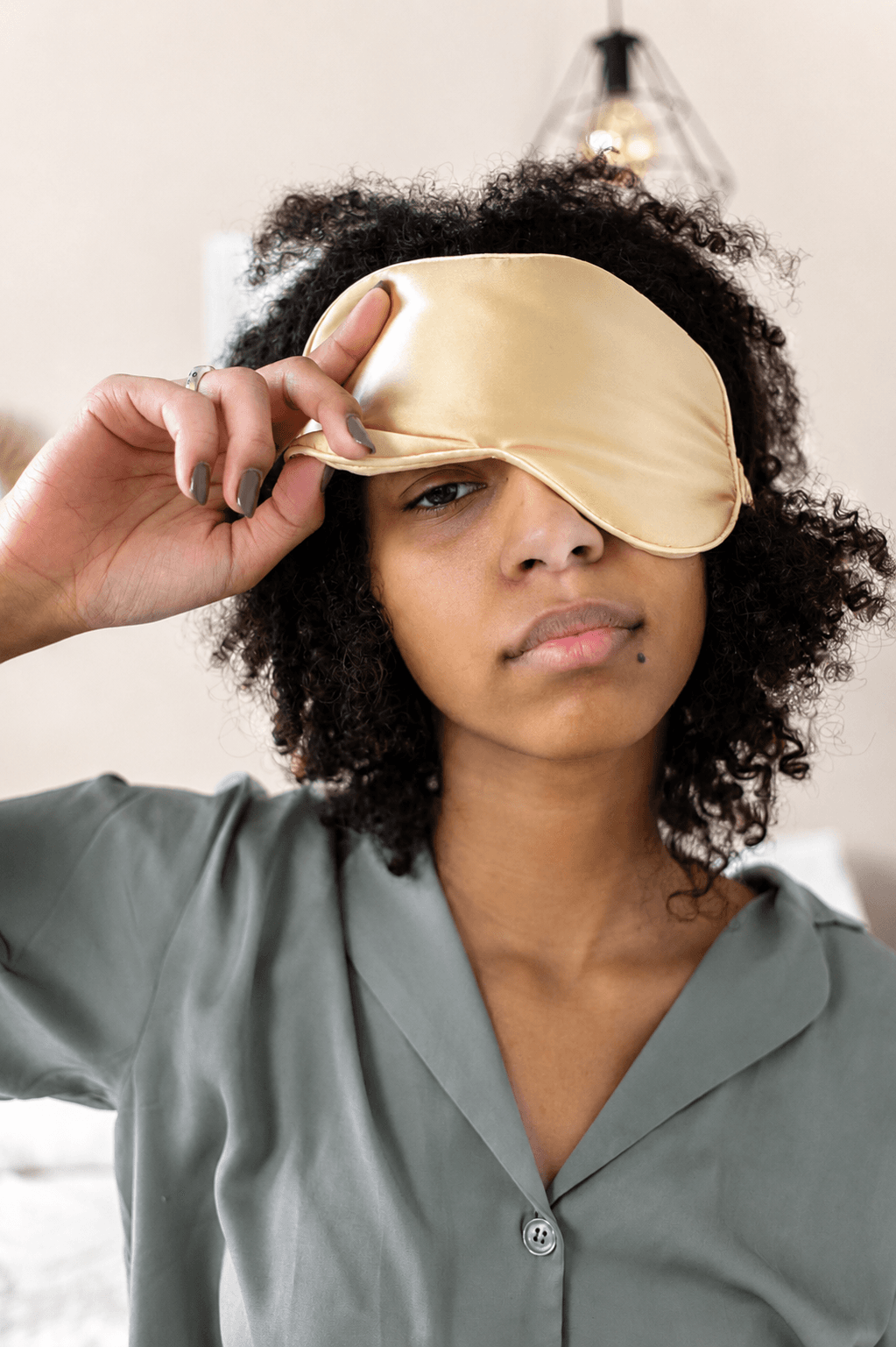 Tired looking woman in pajamas, peeking out of her sleeping mask.