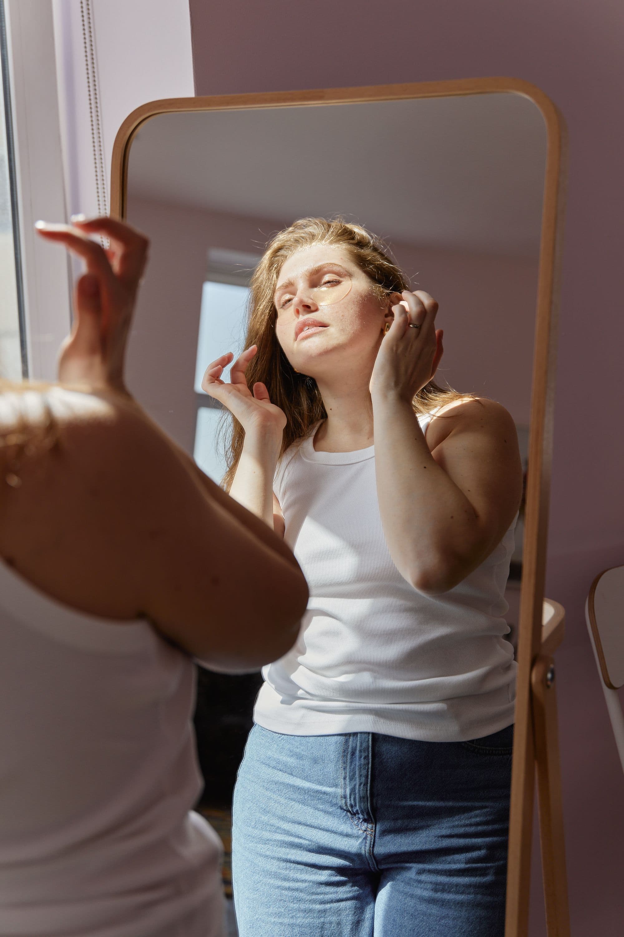 Woman standing in front of mirror applying undereye patches