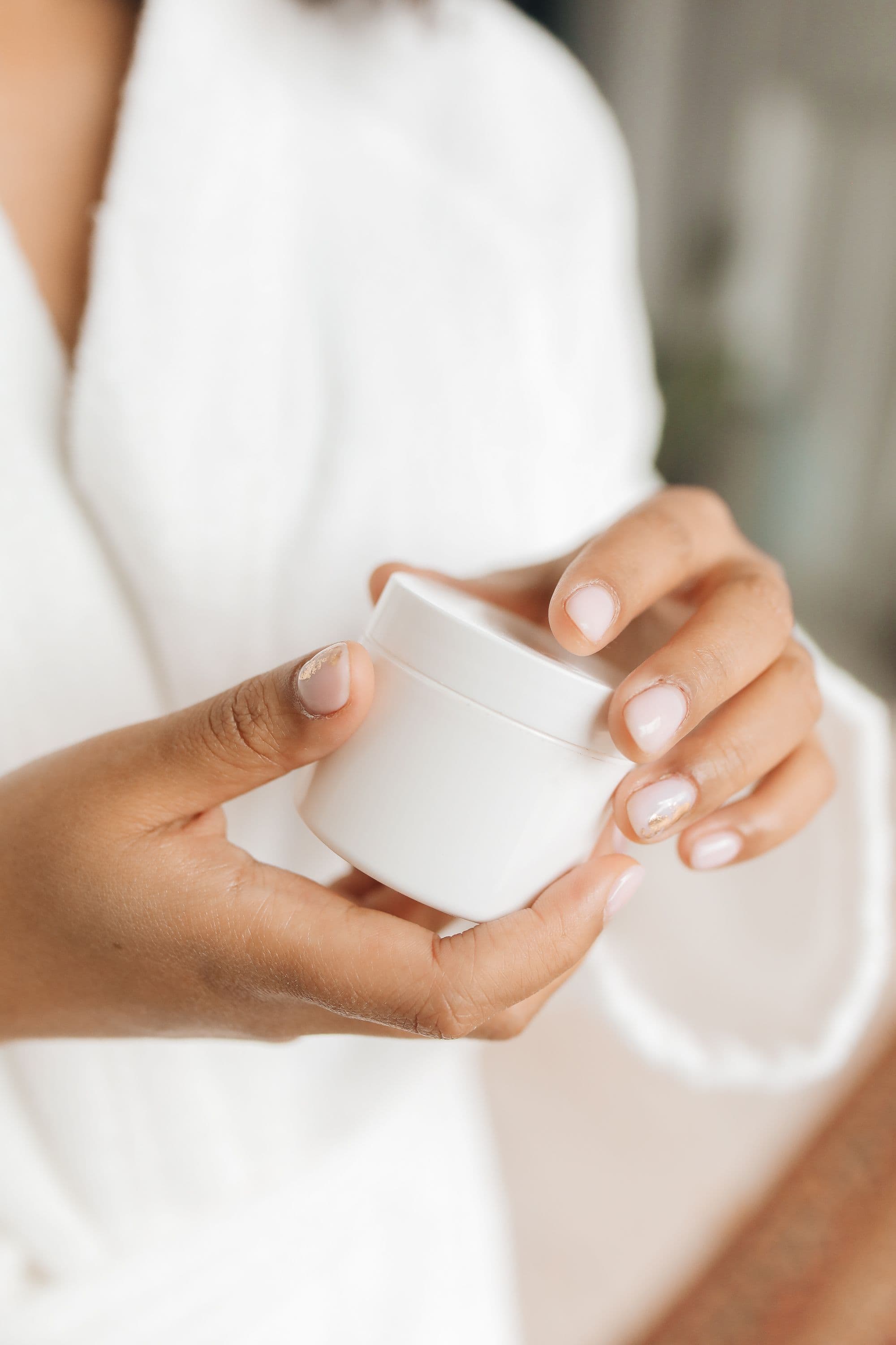 A small white cosmetic container being held in woman's hands.