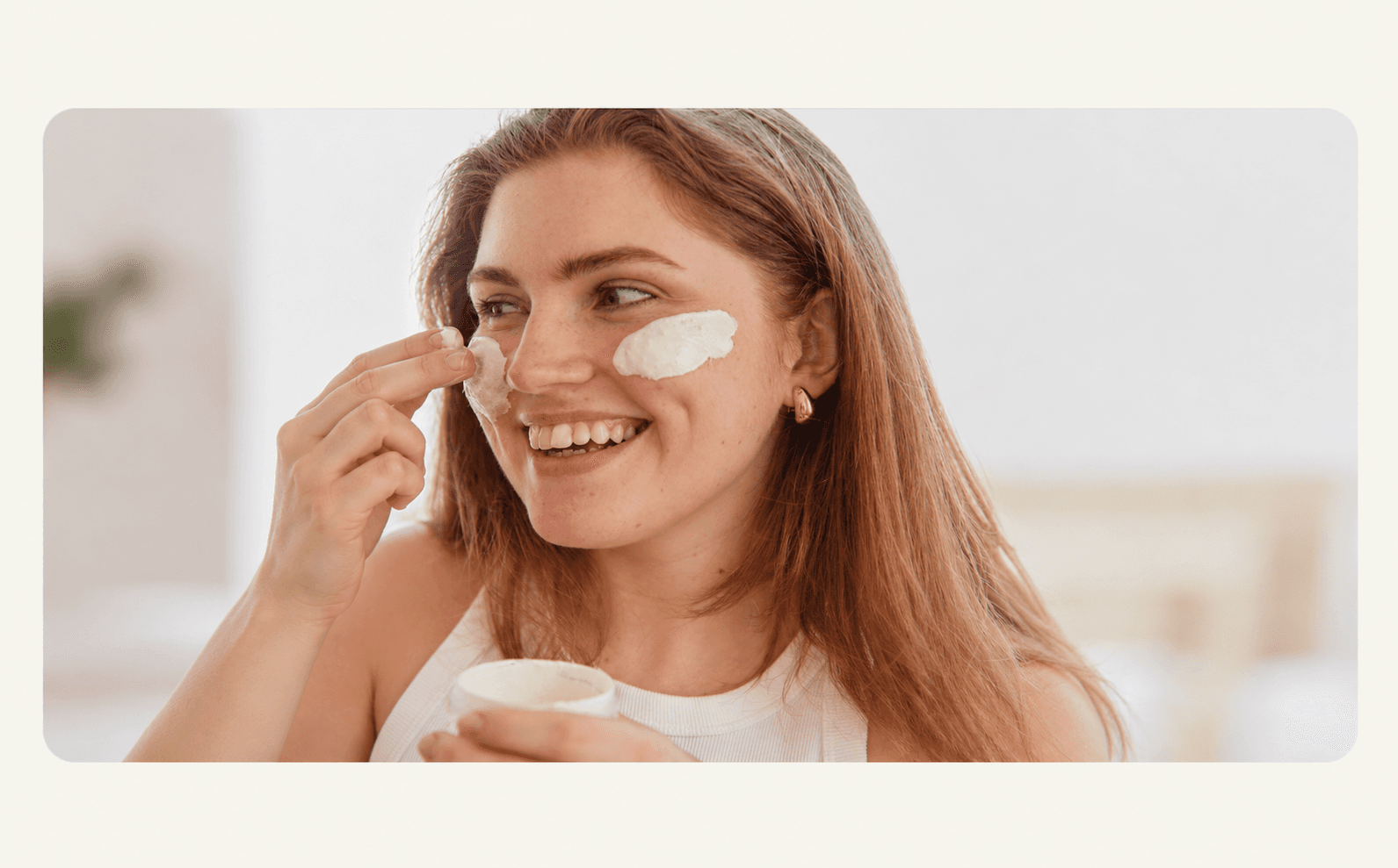 A woman smiling while applying cream to her cheeks.